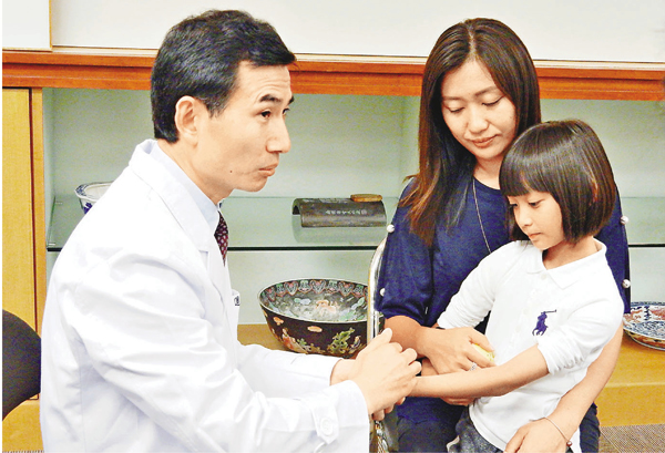 ■孫素明(左一)在子悠手腕示範小兒推拿療法。子悠身後為其母趙太。 黎忞 攝