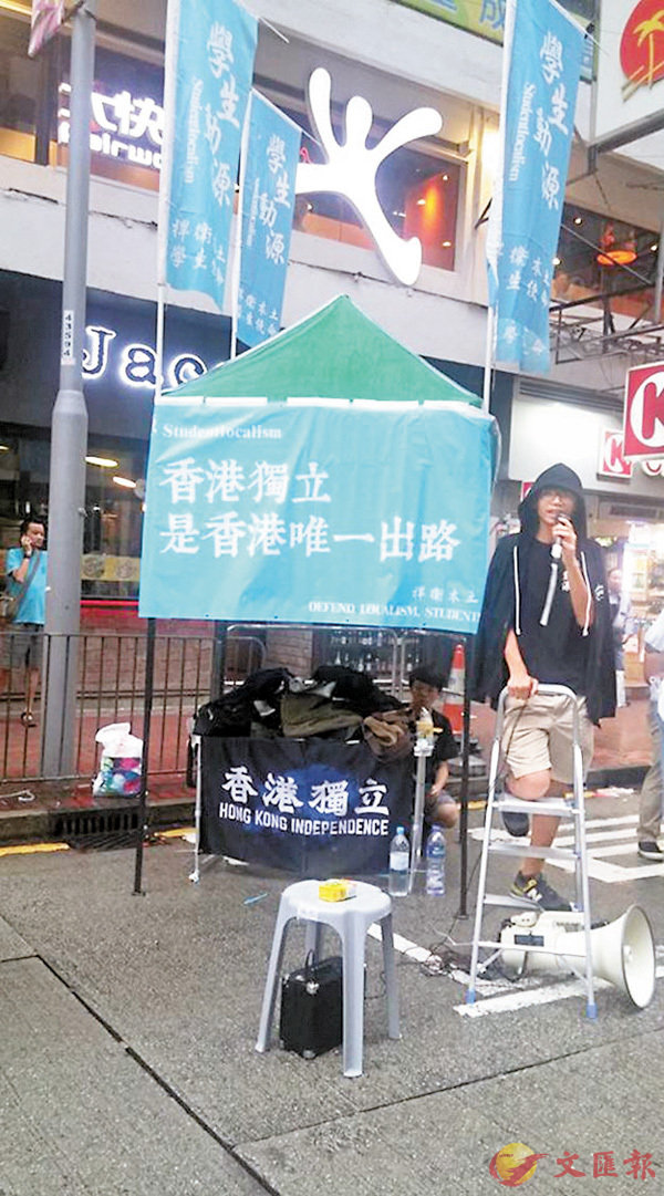 �「學生動源」在「七一遊行」路線上擺街站，照片中展示的黑底白字「香港獨立」旗據知是鍾翰林（披風衣者）5月購自「本土工作室」。fb截圖