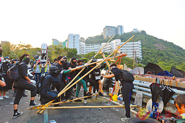 ■中大學生會幹事會臨時行政委員會及多個書院學生會近日籌辦所謂「歷史回顧活動」,乘機美化當日「佔校」暴徒為「義士」。圖為去年中大二橋上,黑衣魔用大型投擲器擲磚頭。 資料圖片